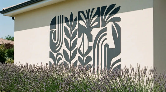 Autocollant extérieur résistant à motif végétal abstrait anthracite posé sur un mur de maison en enduit lisse, en plein soleil, devant un massif de lavande