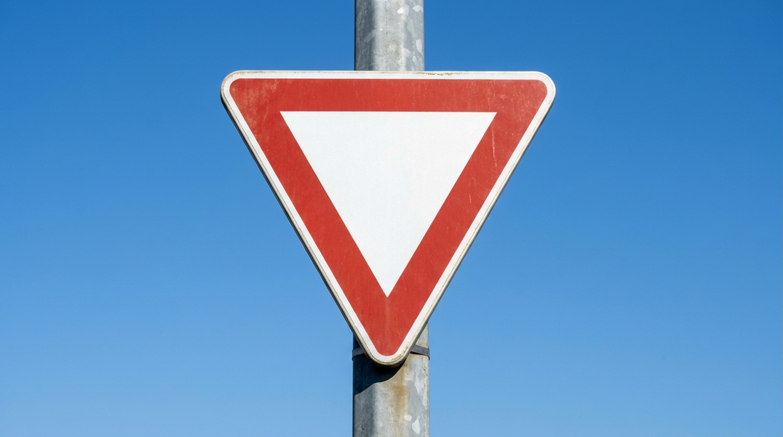 Panneau cédez le passage : triangle pointe en bas à bordure rouge sur un poteau, contre un ciel bleu