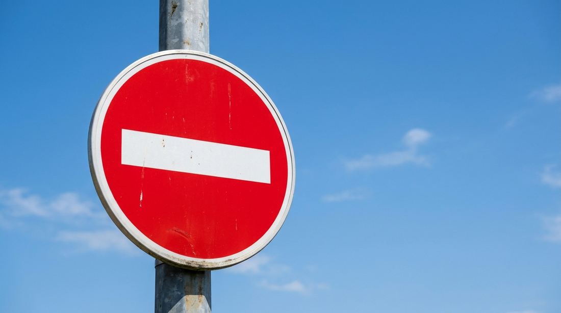 Panneau de sens interdit : disque rouge à bande blanche horizontale sur un poteau, contre un ciel bleu