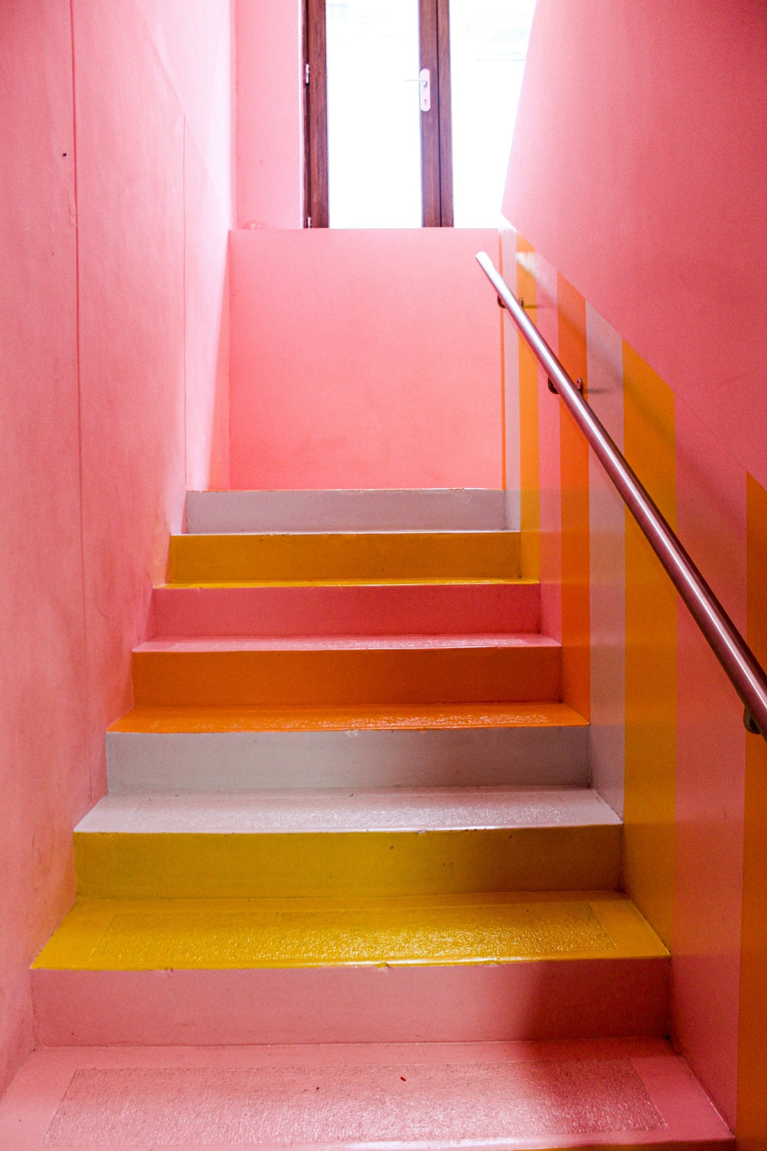 Escalier intérieur dont les contremarches sont habillées de jaune, d'orange et de rose, exemple de sticker d'escalier