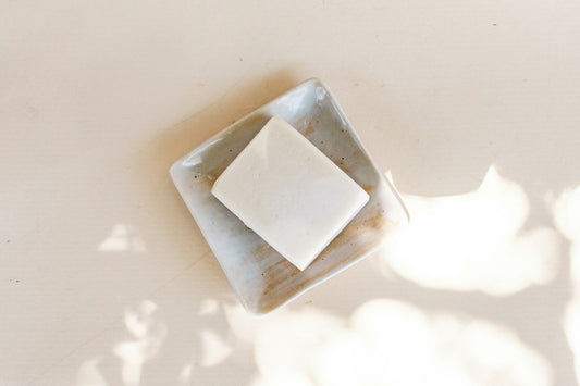 Pain de shampoing solide posé sur un porte-savon en céramique
