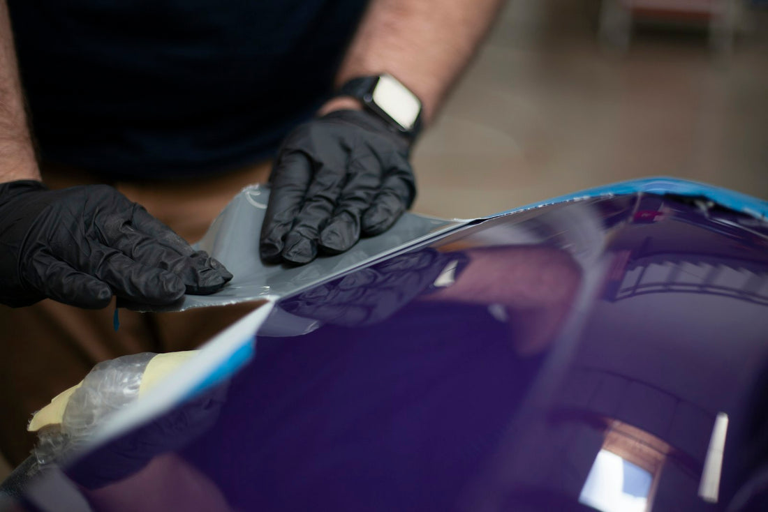 Mains gantées marouflant un film vinyle adhésif sur la carrosserie d'une voiture lors de la pose d'un sticker