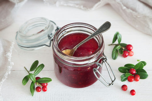 Pot de confiture maison ouvert avec une cuillère, entouré de fruits rouges frais sur un plan blanc, sans étiquette ni marque