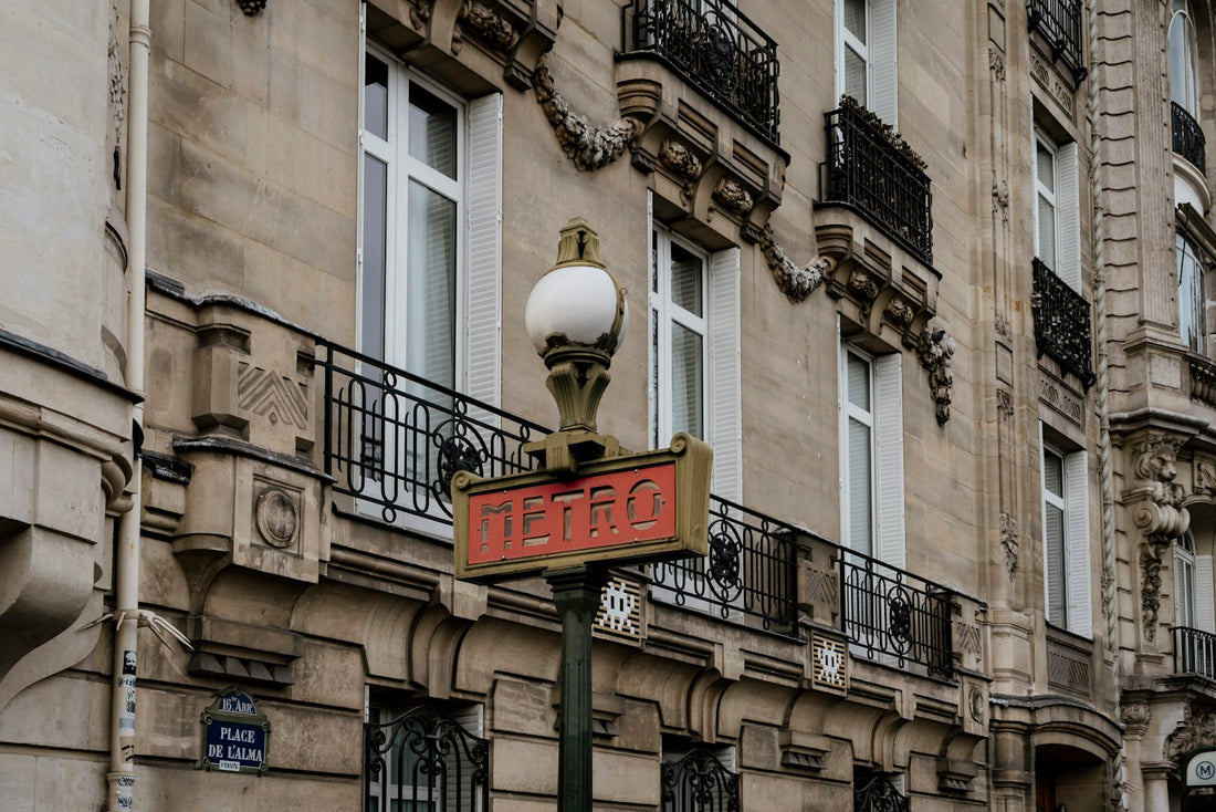 Façade haussmannienne parisienne avec une plaque de rue émaillée bleue « Place de l'Alma » et un mât Métro