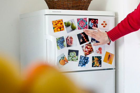 Photos aimantées de fruits disposées sur la porte d'un réfrigérateur, une main ajustant l'un des aimants