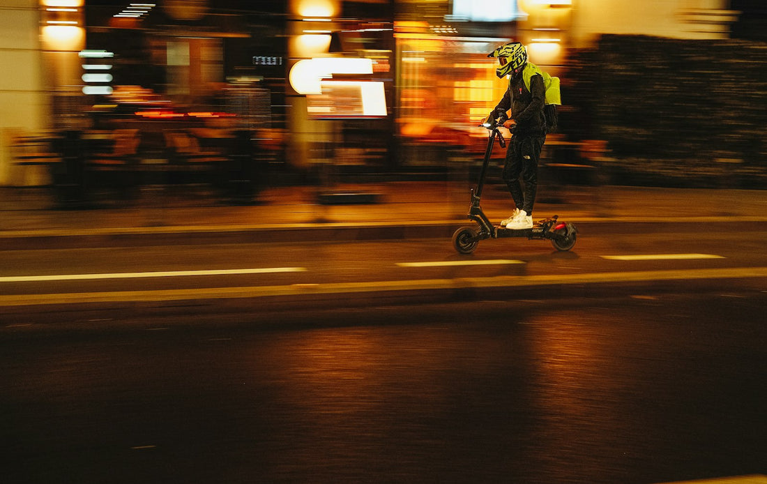 Utilisateur de trottinette électrique en gilet réfléchissant roulant de nuit en ville.