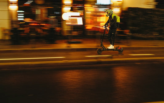 Utilisateur de trottinette électrique en gilet réfléchissant roulant de nuit en ville.