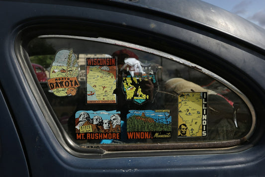 Vitre latérale d'une voiture ancienne décorée d'autocollants de voyage, exemple de sticker posé sur une vitre de voiture.