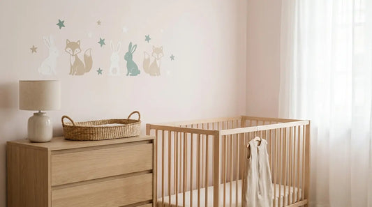 Stickers de chambre bébé représentant des lapins, des renards et des étoiles au-dessus d'une commode en bois clair, sur un mur rose poudré.